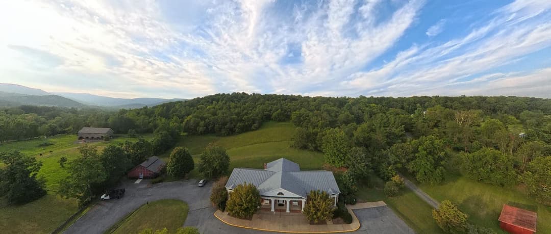 An aerial view of the library and the Book Barn among pasture and woodland, with the Blue Ridge on the horizon.
